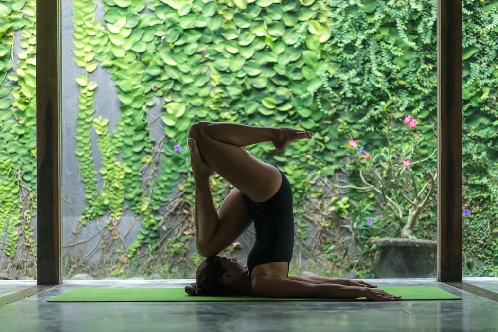 vue latérale de la jeune femme sportive pratiquant le yoga à l'entrée de la pose de la Souffle (Halasana) devant le mur recouvert de feuilles vertes
 - Photo, image