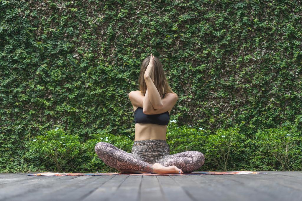 jovem atraente praticando ioga em pose de lótus na frente da parede coberta com folhas verdes
 - Foto, Imagem