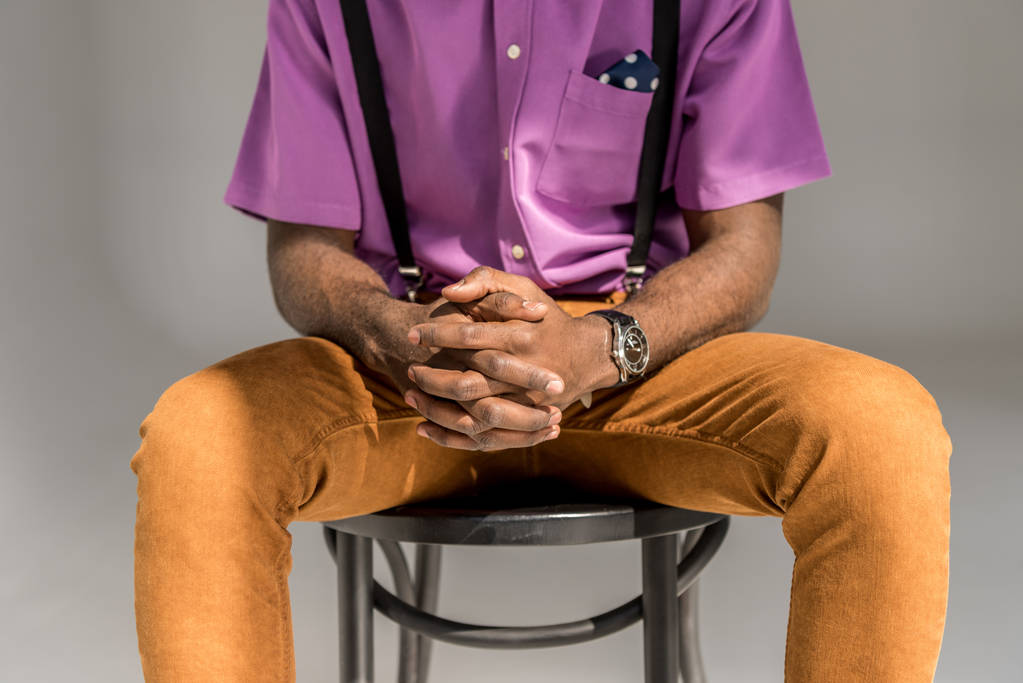 colpo ritagliato di uomo afroamericano con le mani in serratura seduto sulla sedia isolata su grigio
 - Foto, immagini