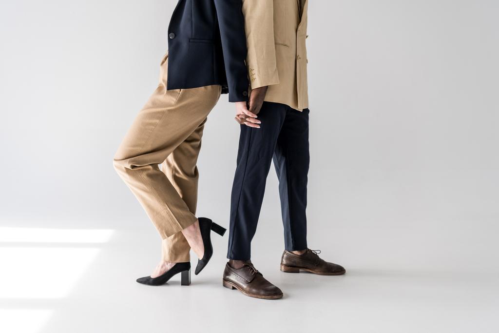 corte tiro de elegante jovem casal multiétnico de pé de volta para trás e de mãos dadas em cinza
 - Foto, Imagem