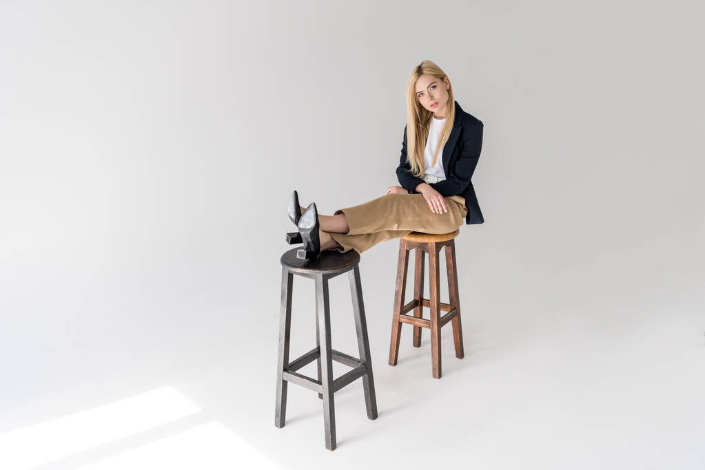 красивая стильная молодая женщина сидит на стульях и смотрит в камеру на сером
  - Фото, изображение