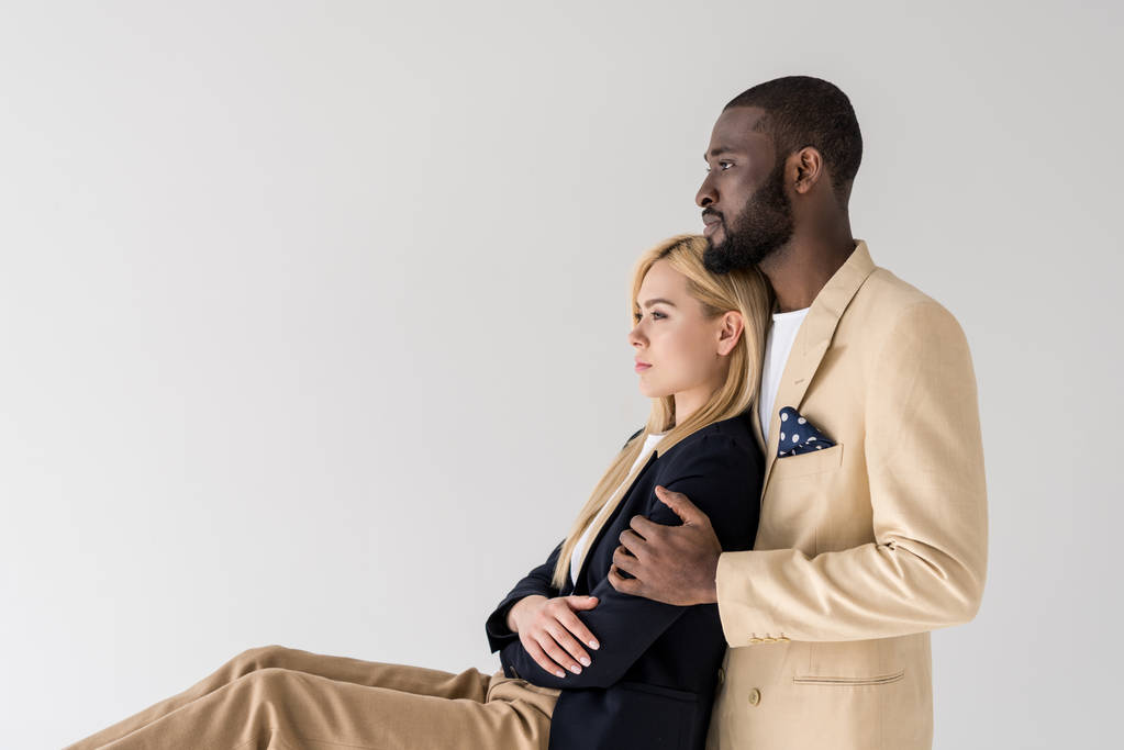 Вид сбоку на модную молодую многонациональную пару, сидящую и отводящую взгляд в сторону от серого
 - Фото, изображение