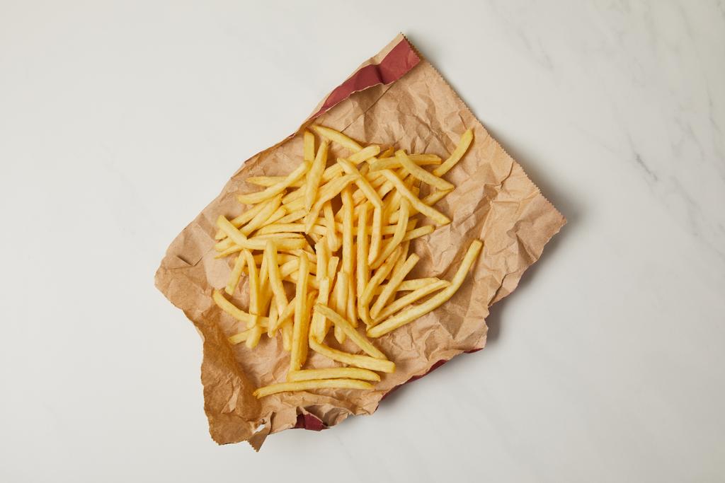 bovenaanzicht van heerlijke frietjes overgeslagen verfrommeld papier op wit - Foto, afbeelding