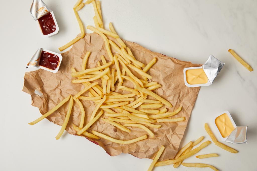 top view of french fries on crumpled paper with containers of sauces on white - Photo, Image