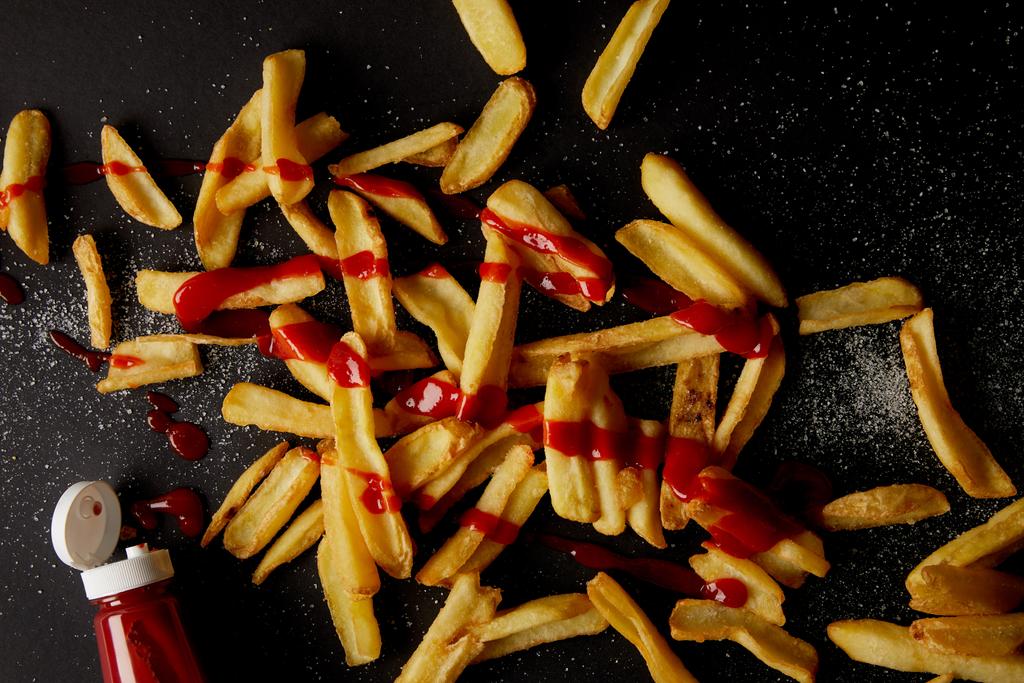 vista superior de deliciosas batatas fritas derramadas com sal e derramadas com ketchup em preto
 - Foto, Imagem