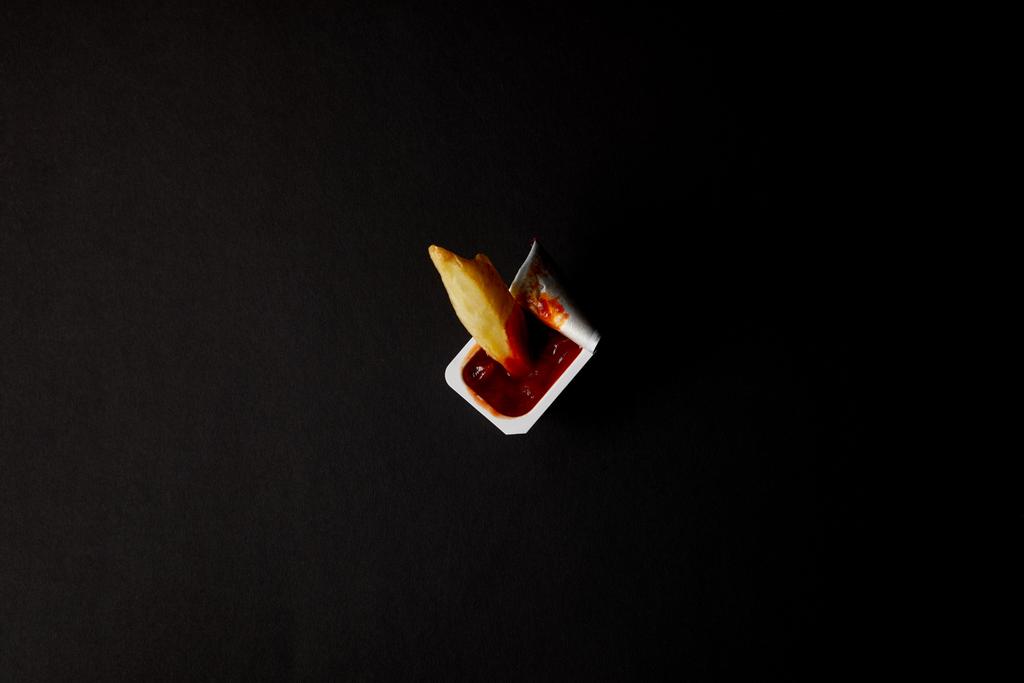 vista dall'alto del contenitore di plastica con ketchup con patate fritte versate isolate sul nero
 - Foto, immagini