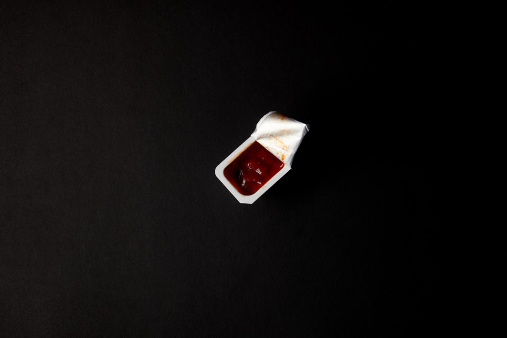 bovenaanzicht van kunststof container met ketchup geïsoleerd op zwart - Foto, afbeelding
