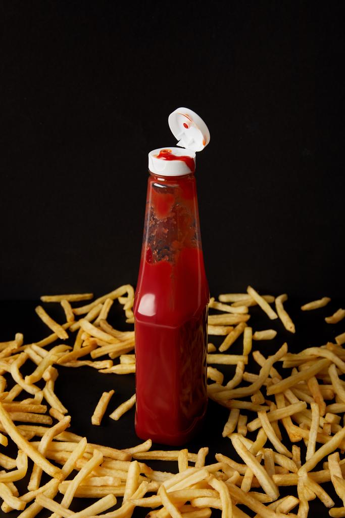 bottle of ketchup surrounded with french fries isolated on black - Photo, Image