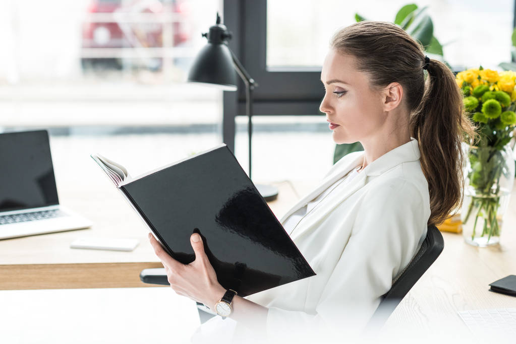 side view of beautiful businesswoman with book at workplace in office - Photo, Image