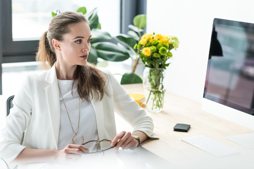 kobieta kobieta interesu, patrząc na ekran komputera w miejscu pracy z bukiet kwiatów w wazonie w biurze - Zdjęcie, obraz