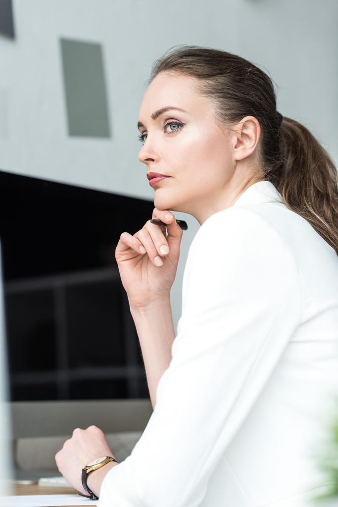 side view of beautiful pensive businesswoman in white suit looking away in office - Photo, Image