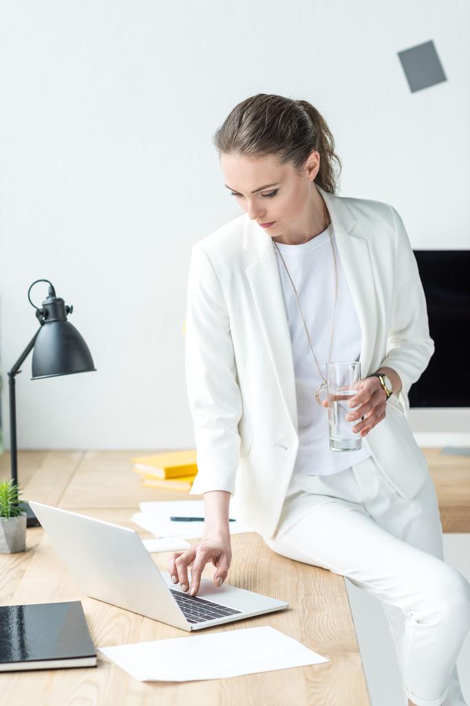 zakenvrouw met glas water bezig met laptop op werkplek op kantoor - Foto, afbeelding