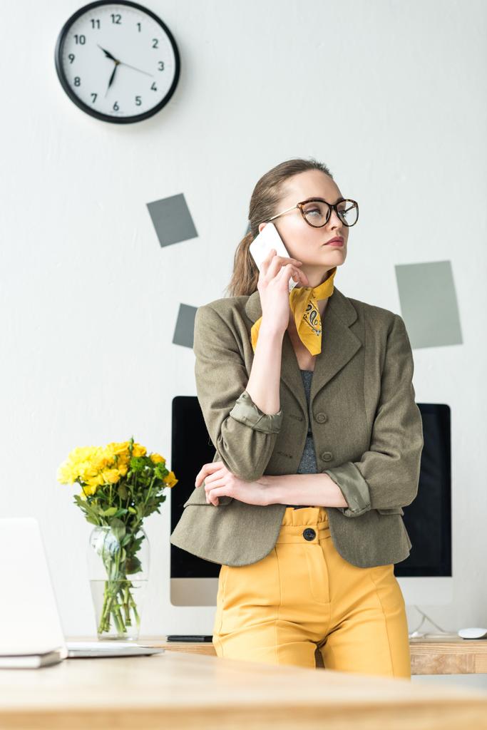 ελκυστικός επιχειρηματίας σε γυαλιά μιλώντας από smartphone και κοιτώντας μακριά στο γραφείο - Φωτογραφία, εικόνα
