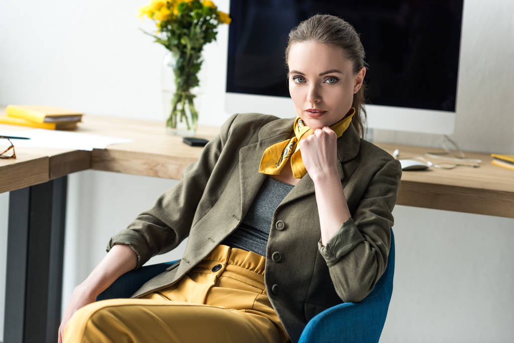 beautiful stylish businesswoman sitting at workplace and looking at camera  - Photo, Image