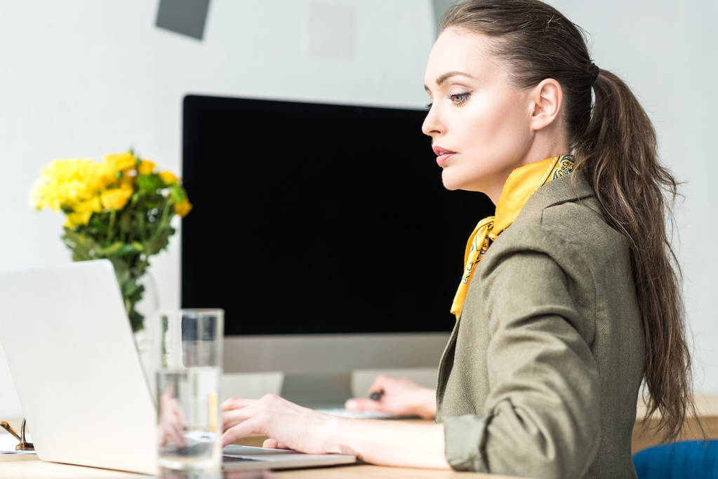 боковой вид привлекательной стильной бизнесвумен с ноутбука в офисе
 - Фото, изображение