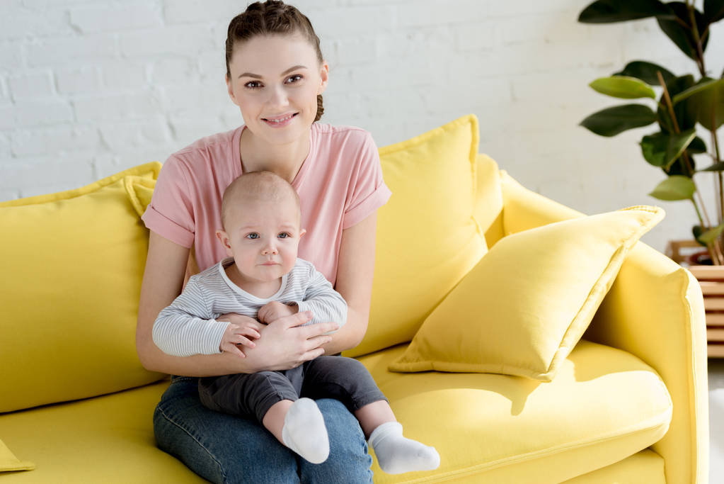 jovem sorridente mãe com pequeno filho sentado no sofá
 - Foto, Imagem