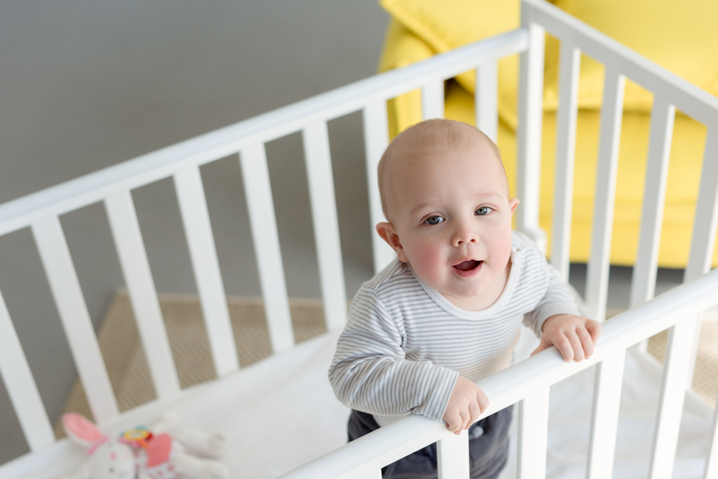 niño feliz de pie en la cuna del bebé
 - Foto, imagen