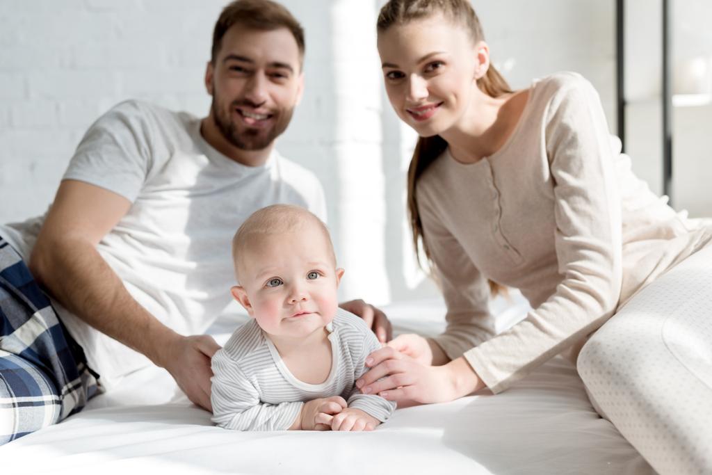 uśmiechający się rodzice z małym synem na łóżku - Zdjęcie, obraz