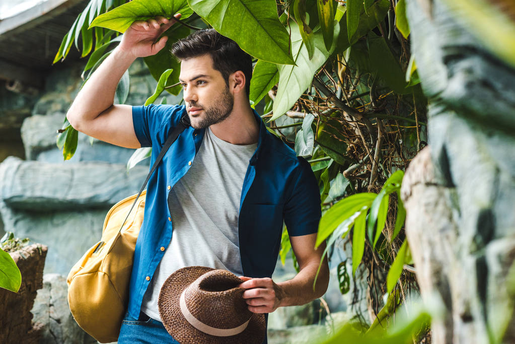 handsome young man in stylish clothes with straw hat in rainforest - Photo, Image