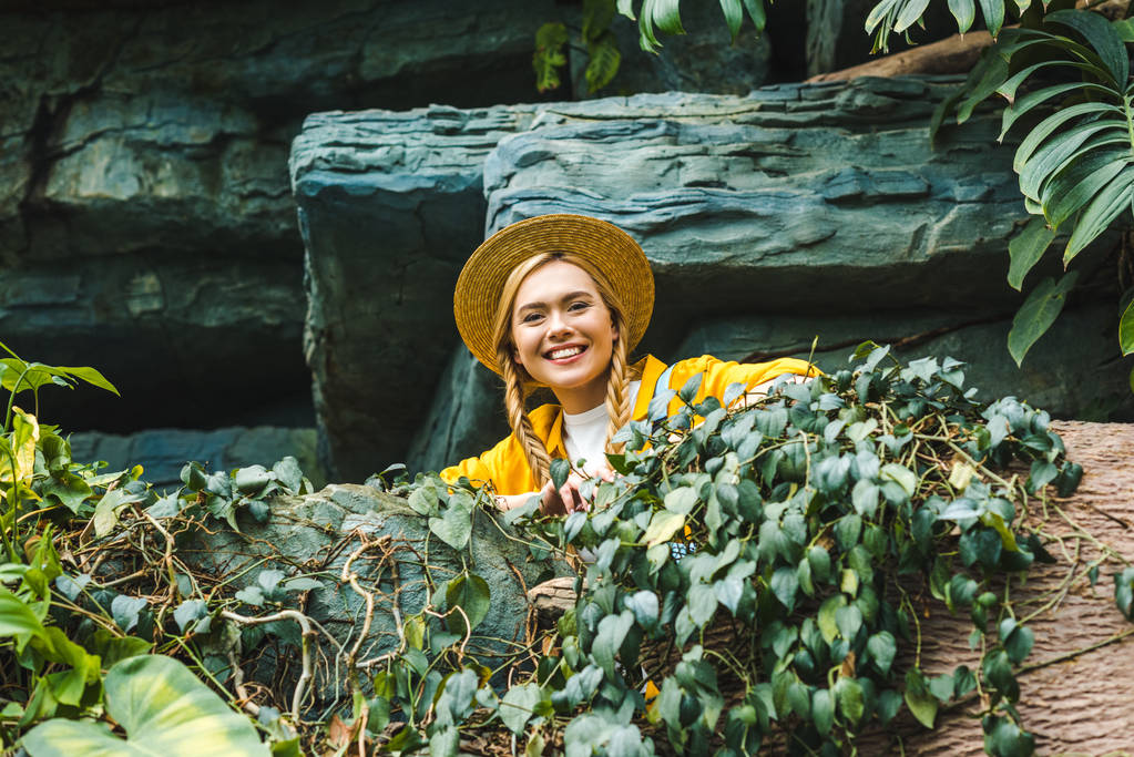 bottom view of happy young woman in straw hat looking at camera in jungle - Photo, Image
