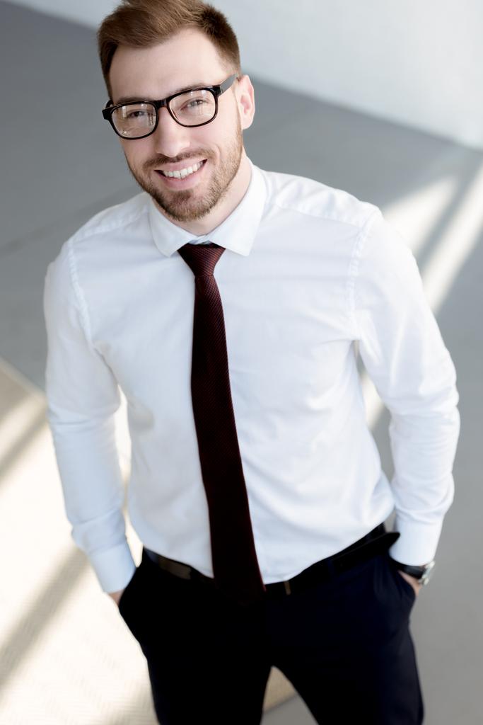 Lächelnder Geschäftsmann mit Brille posiert nahe weißer Wand - Foto, Bild