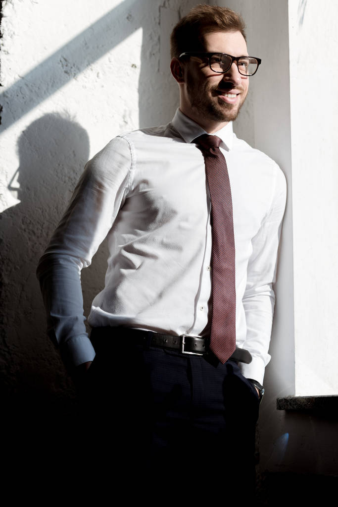 счастливый бизнесмен в галстуке и в очках, позирующих возле белой стены
 - Фото, изображение