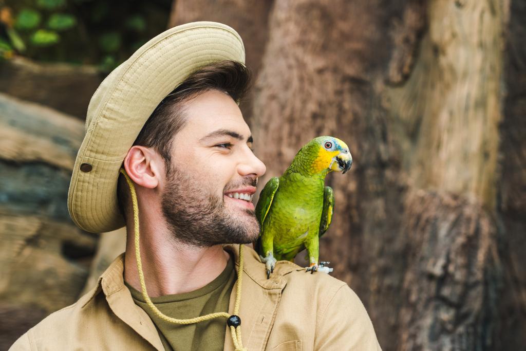 όμορφος νεαρός άνδρας με παπαγάλο στον ώμο στη ζούγκλα - Φωτογραφία, εικόνα