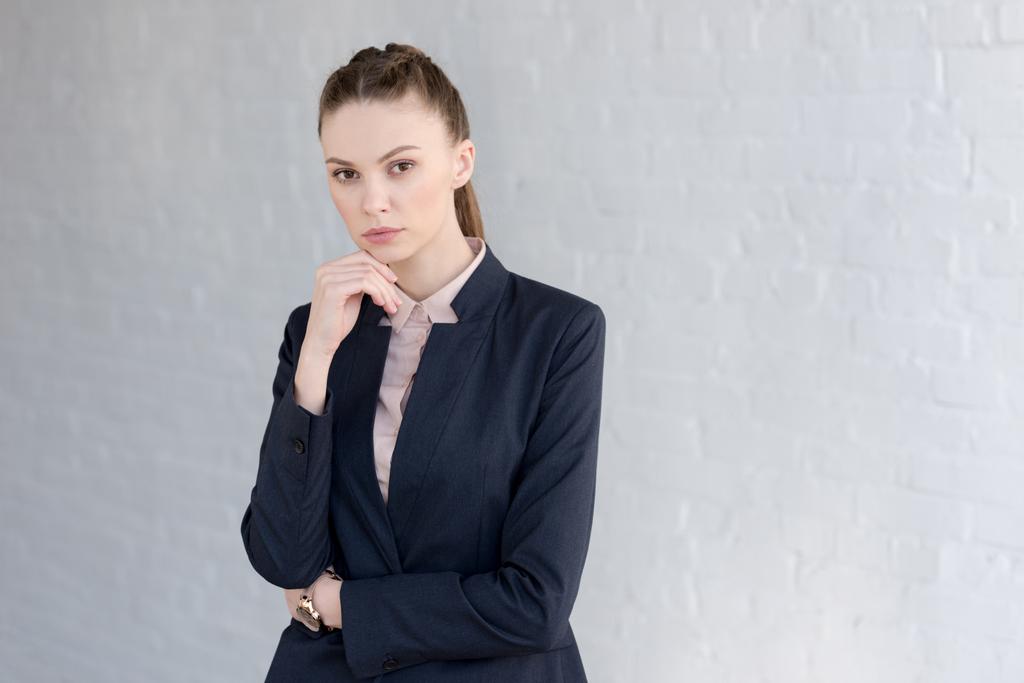 задумчивая деловая женщина в формальной одежде позирует возле белой стены
  - Фото, изображение