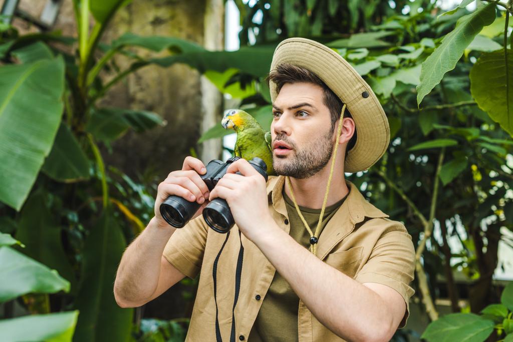 wstrząśnięty, młody człowiek z papugą na ramieniu i lornetki w dżungli - Zdjęcie, obraz