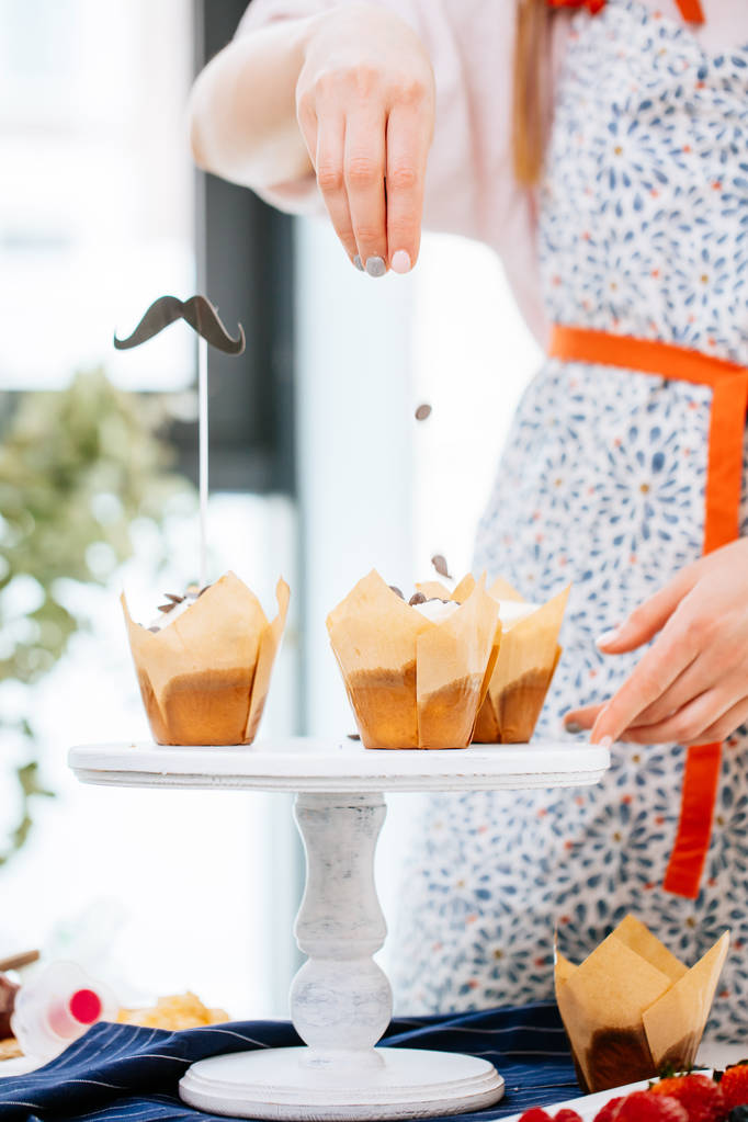 lähikuva leivonnainen nainen käsi koristelu cupcakes suklaa sprinkles keittiössä
 - Valokuva, kuva
