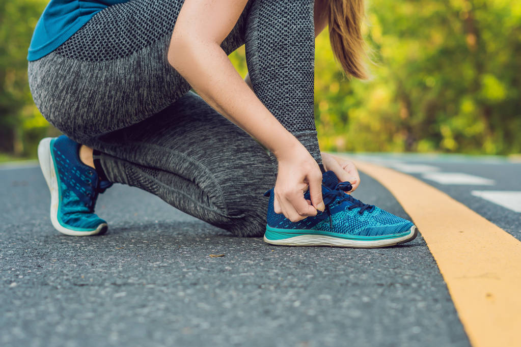 Läuferin bindet ihre Schuhe weiß und bereitet sich auf das Joggen draußen vor. junge Läuferin bereitet sich auf das Training vor. Sportlicher Lebensstil. - Foto, Bild