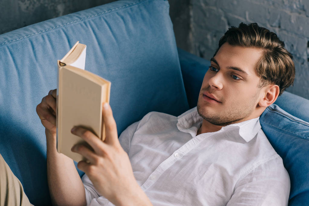 Jonge man thuis ontspannen op de sofa met boek - Foto, afbeelding