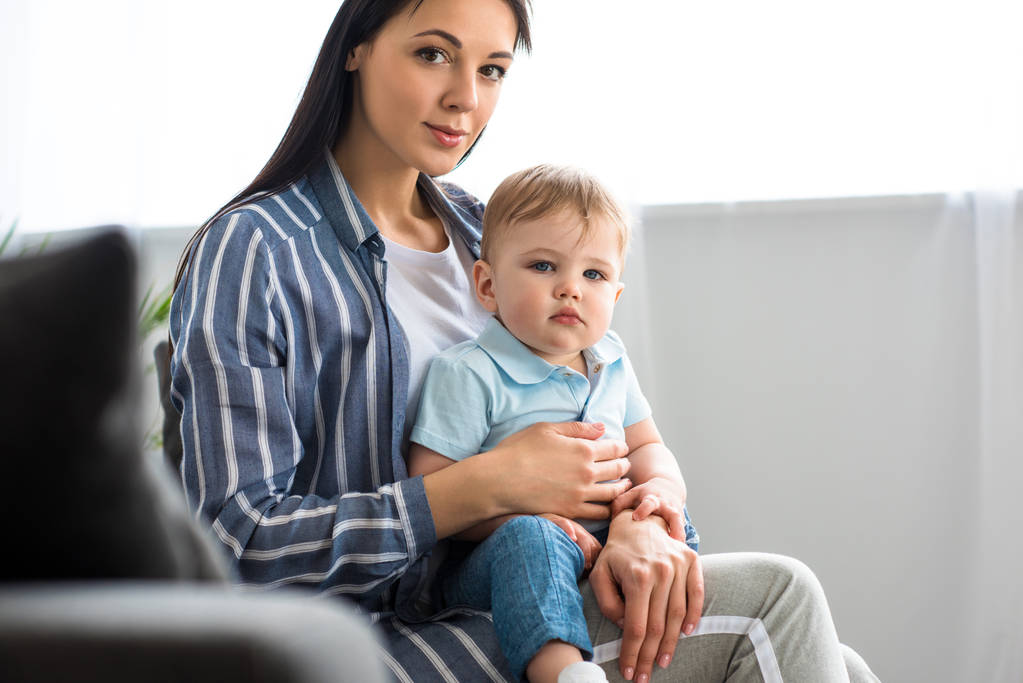 matka s rozkošný chlapeček na ruce sedí na gauči doma - Fotografie, Obrázek