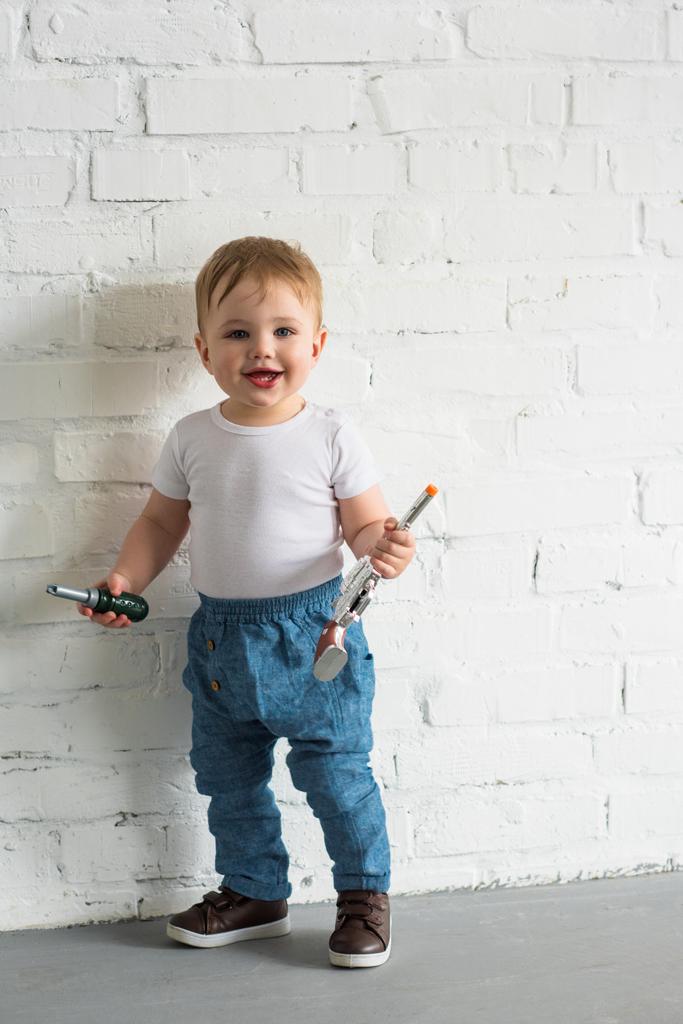 白いレンガの壁に立っているおもちゃで幸せな男の子 ロイヤリティフリー写真 画像素材