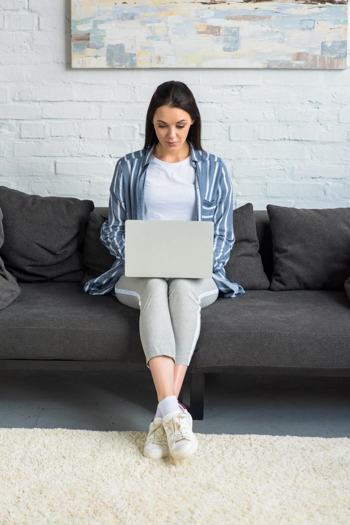 Jovem mulher usando laptop no sofá em casa
 - Foto, Imagem