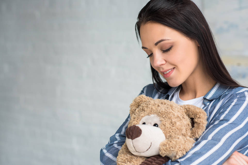 Porträt einer lächelnden attraktiven Frau mit Teddybär zu Hause - Foto, Bild