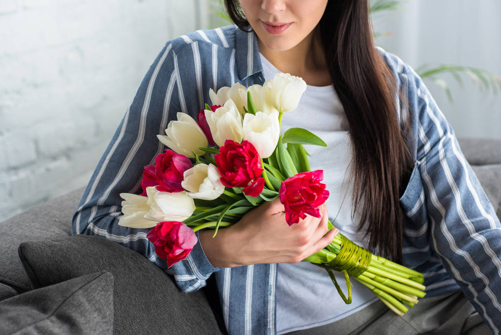 przycięte strzał z piękną kobietą w ręku trzymając bukiet tulipanów, siedząc na kanapie - Zdjęcie, obraz