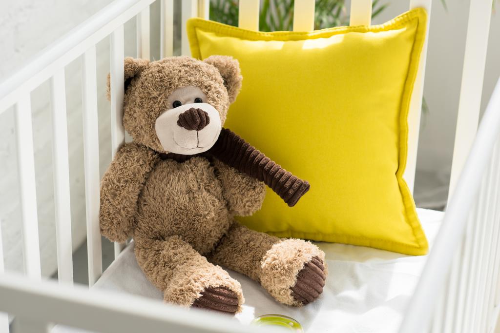 Nahaufnahme von Teddybär und gelbem Kissen im Kinderbett zu Hause - Foto, Bild