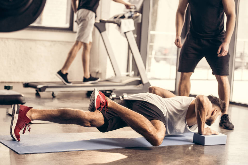 imagen recortada de entrenador de pie cerca de deportista haciendo tablón en bloques de yoga en el gimnasio
 - Foto, Imagen