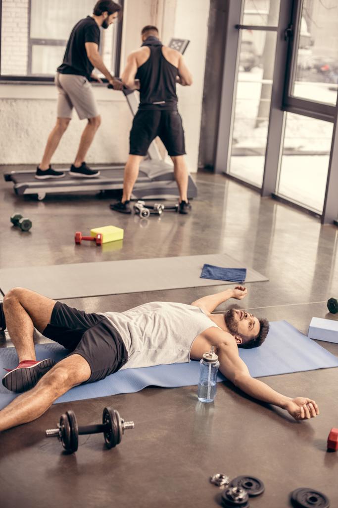handsome tired sportsmen lying on yoga mat in gym - Photo, Image