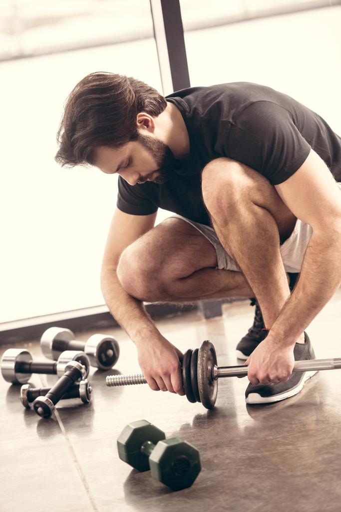 desportista bonito colocando placas de peso na barra de ferro para treinamento em ginásio
 - Foto, Imagem