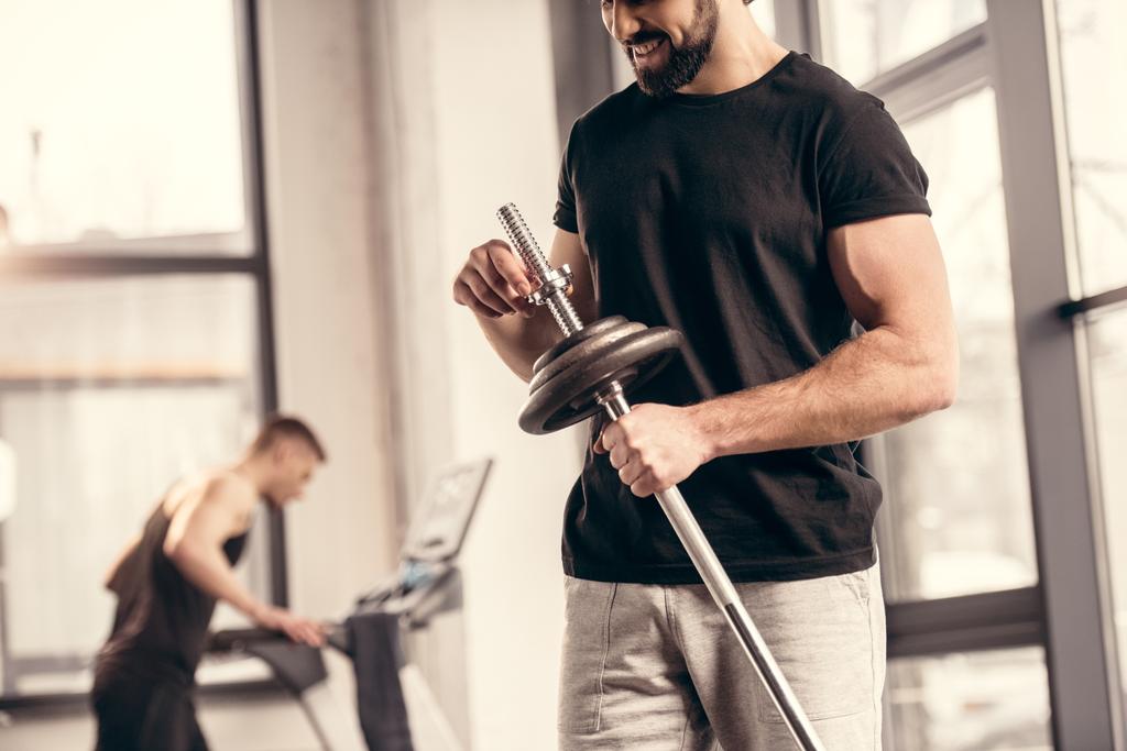 abgeschnittenes Bild eines Sportlers, der Hantelscheiben an Eisenstange für das Training im Fitnessstudio befestigt - Foto, Bild