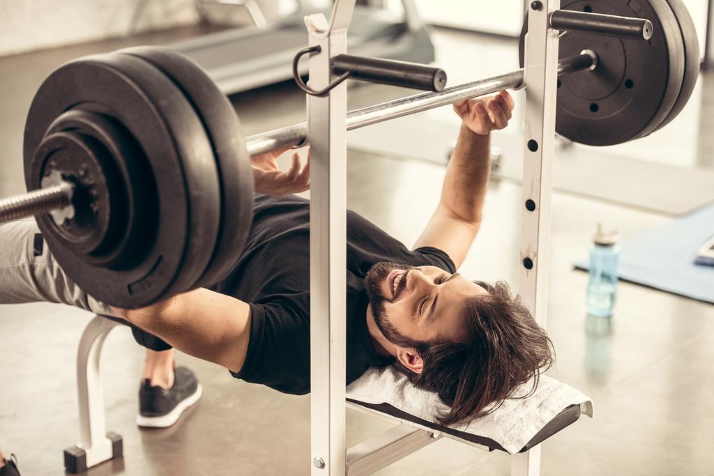 beau sportif souriant préparant haltère de levage sur banc presse dans la salle de gym
 - Photo, image
