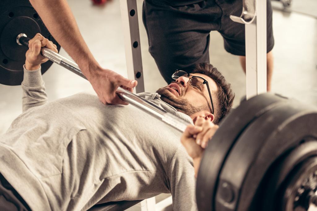 abgeschnittenes Bild eines Trainers, der Sportlern beim Heben schwerer Gewichte im Fitnessstudio hilft - Foto, Bild