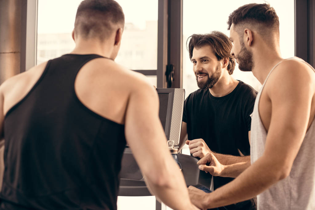 smiling handsome sportsmen near treadmill in gym - Photo, Image