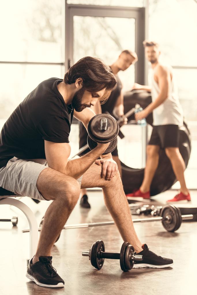Seitenansicht eines gut aussehenden, muskulösen Mannes beim Training mit Kurzhanteln im Fitnessstudio - Foto, Bild