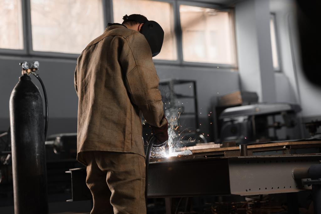 Rückansicht des Fertigungsarbeiters beim Schweißen von Metall mit Funken in der Fabrik  - Foto, Bild