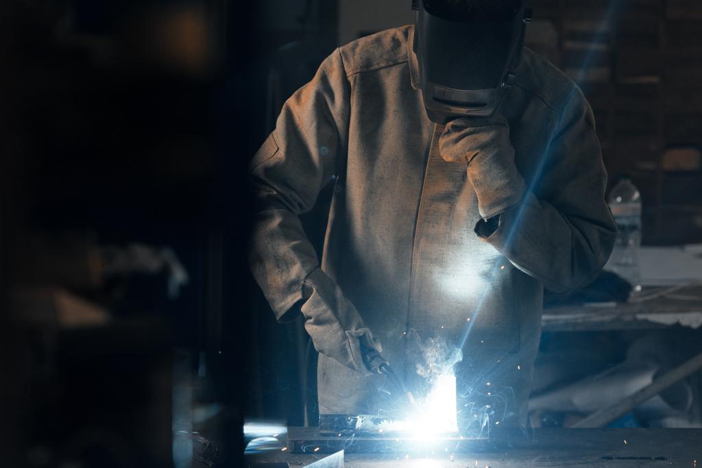 сварщик в защитной маске, работающий с металлом на заводе
  - Фото, изображение