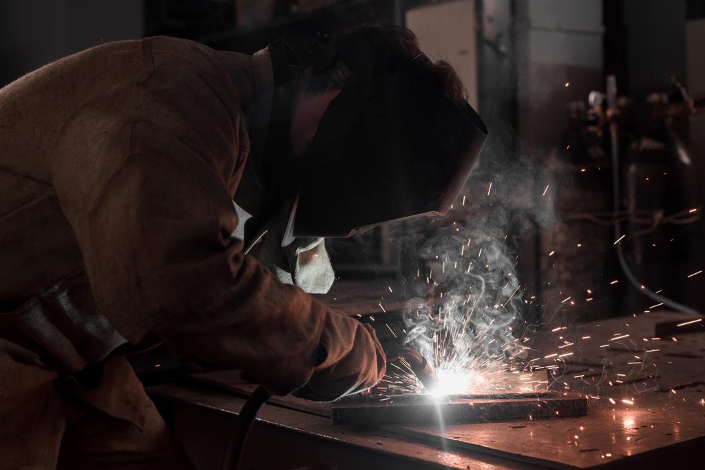 visão lateral do trabalhador em proteção máscara de soldagem de metal na fábrica
  - Foto, Imagem