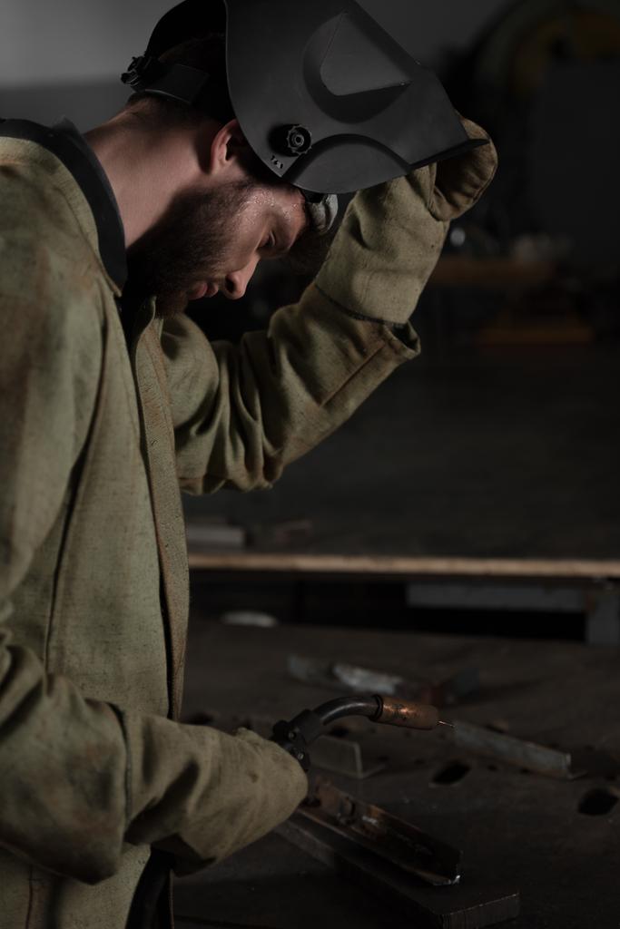 visão lateral do soldador levantando máscara protetora para olhar para o seu trabalho
  - Foto, Imagem